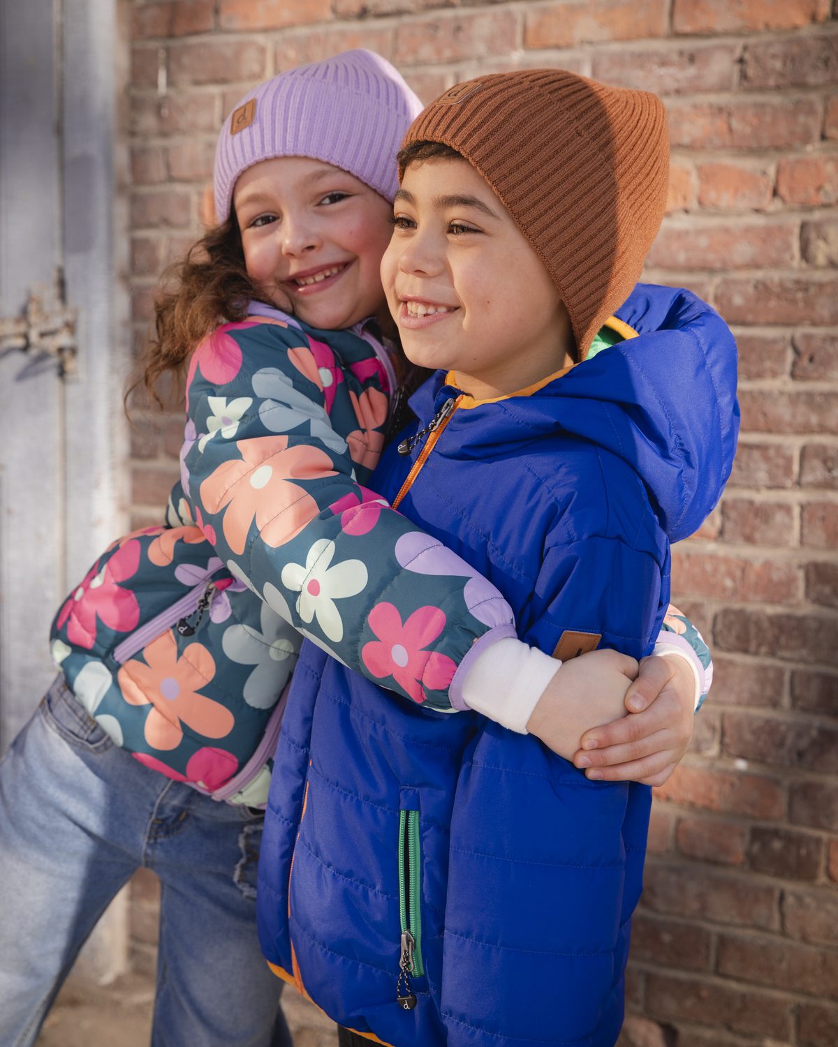 Two kids hugging in Deux par Deux floral and blue puffer coats