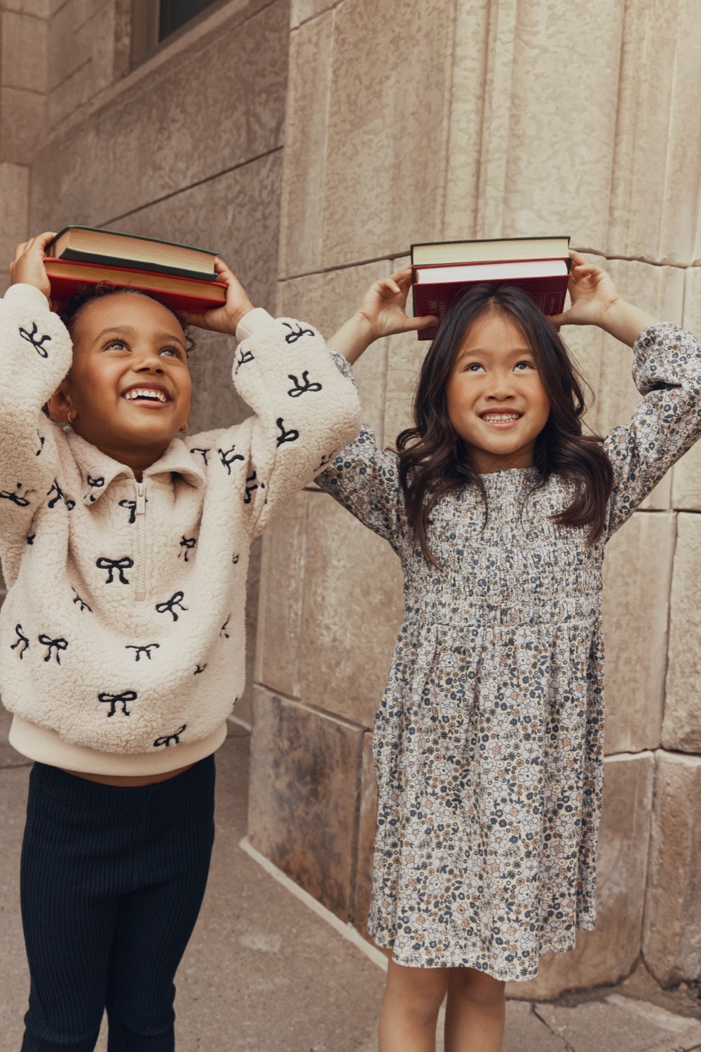 Boy in a Miles The Label bow-print sherpa quarter-zip and girl in a floral dress, books balanced on their heads
