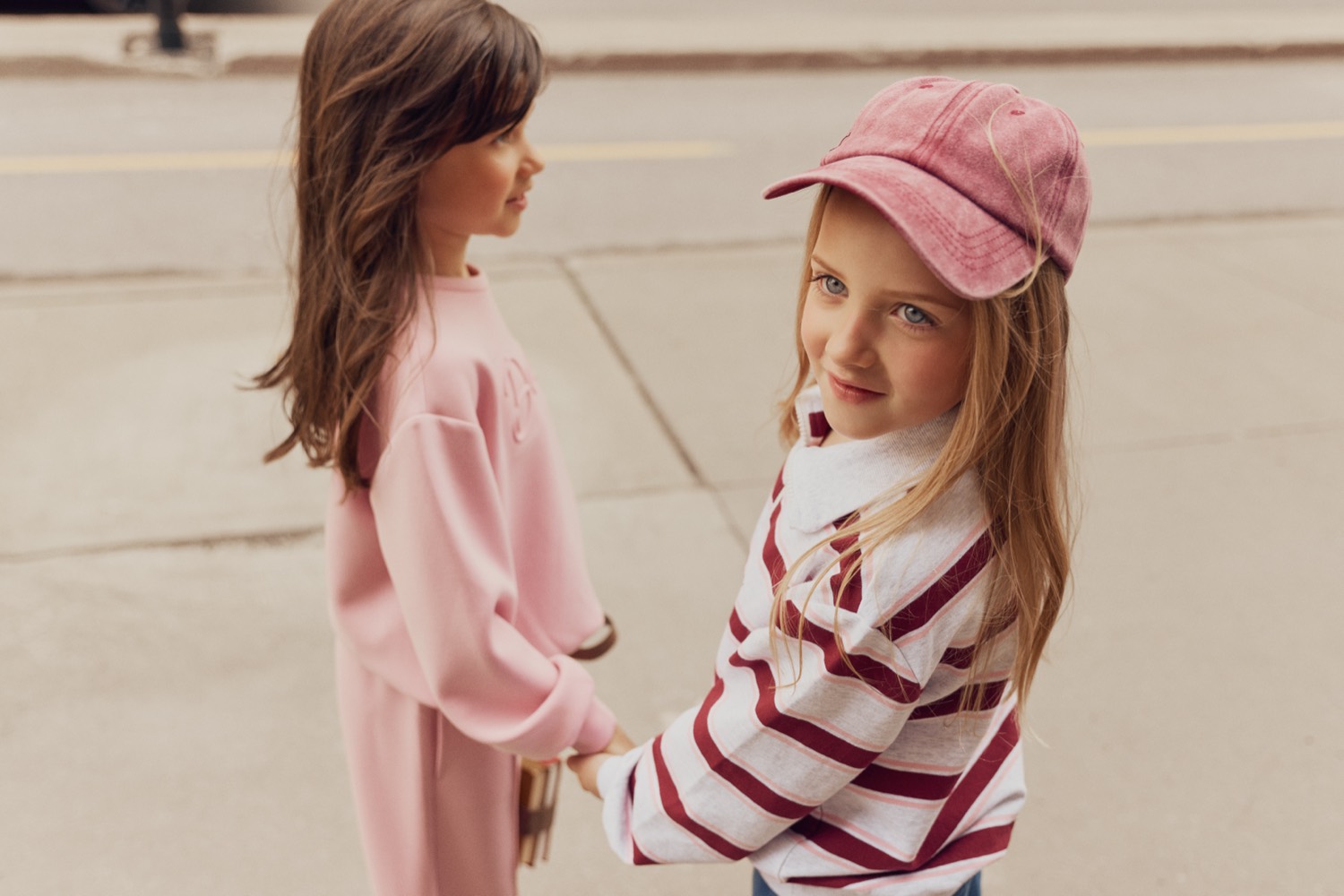 Two girls in a Miles The Label pink sweatsuit and burgundy-striped rugby top