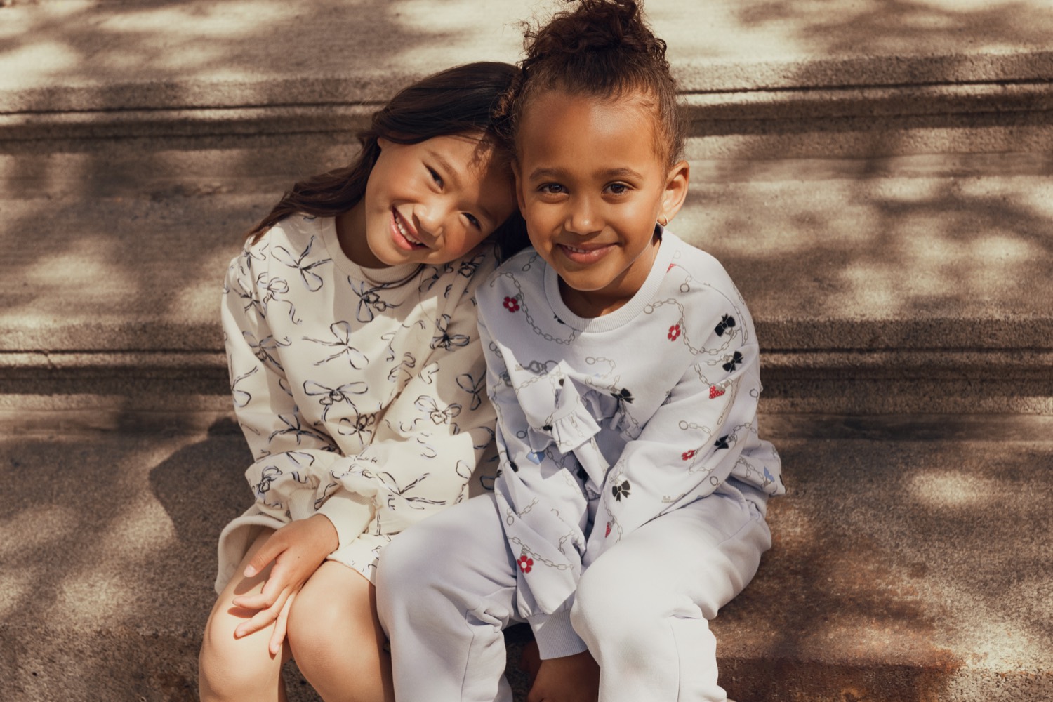 Two girls sitting together in Miles The Label bow-print and floral loungewear